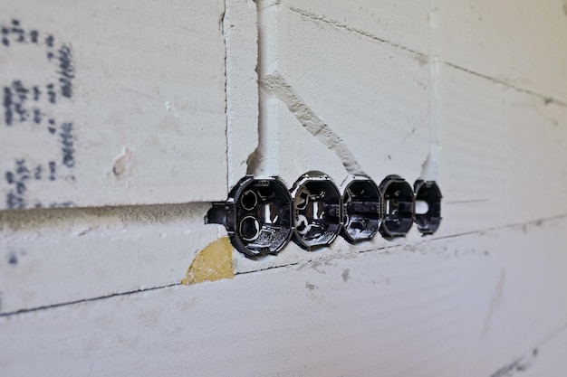 Foto caixas de plástico pretas com buracos redondos para cabos e tomadas elétricas instaladas em uma casa nova, detalhe de parede vazia.