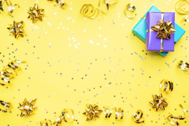 Caixas de presente com fitas de ouro e laços, estrelas de confetes sobre um fundo amarelo. Copie o espaço Lay plana. Cartão de felicitações para festa de aniversário, casamento dia das mães.