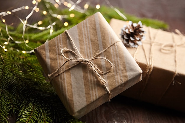 Caixas de presente com luz de Natal e galho de árvore com cones em fundo de madeira marrom