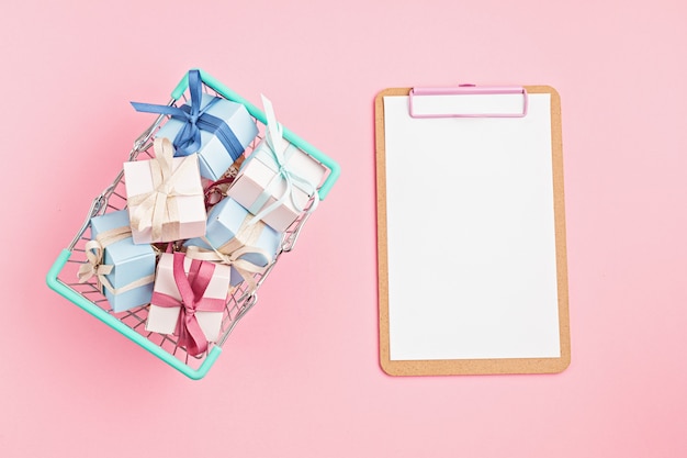 Foto caixas de presente de natal no cesto de compras e prancheta na superfície rosa
