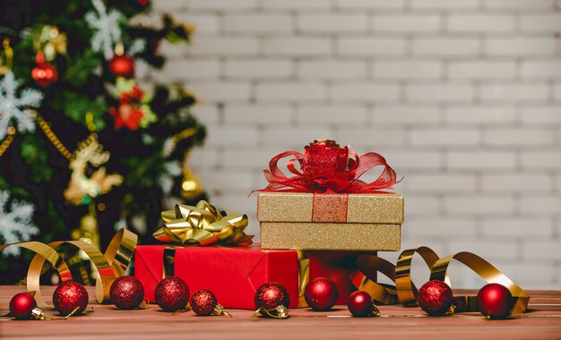 Caixas de presente de presente coloridas com gravata borboleta de fita de cor brilhante colocada no canto da mesa de madeira em frente totalmente decorativo lindo pinheiro de véspera de Natal e parede de tijolos no fundo desfocado.