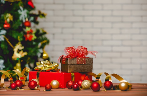 Caixas de presente de presente coloridas com gravata borboleta de fita de cor brilhante colocada no canto da mesa de madeira em frente totalmente decorativo lindo pinheiro de véspera de Natal e parede de tijolos no fundo desfocado.