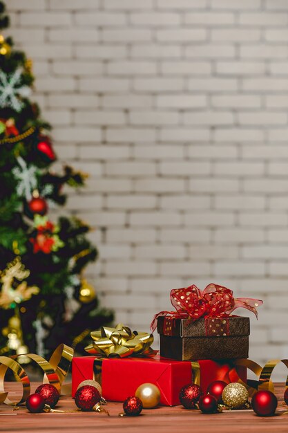 Caixas de presente de presente coloridas com gravata borboleta de fita de cor brilhante colocada no canto da mesa de madeira em frente totalmente decorativo lindo pinheiro de véspera de Natal e parede de tijolos no fundo desfocado.