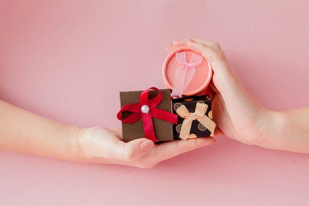 Caixas de presente pequenas nas mãos das mulheres em um fundo rosa. Conceito festivo para dia dos namorados, dia das mães ou aniversário