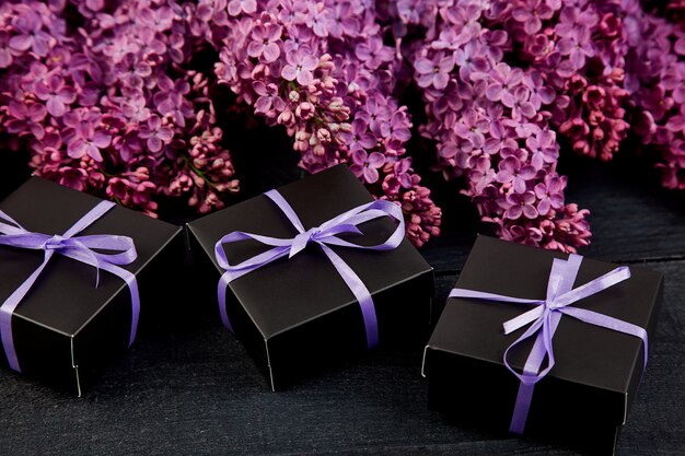 Caixas de presente pequenas pretas embrulhadas fita roxa com lilás natural.