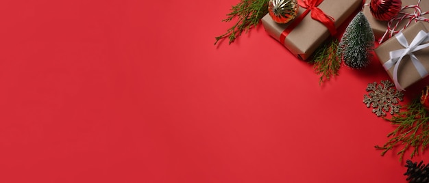 Caixas de presentes, enfeites de Natal e galhos de árvores de abeto em fundo vermelho. Copie o espaço.