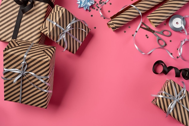 Caixas de presentes marrons listradas de diferentes tamanhos amarradas com fitas e arcos pretos e prateados em um fundo rosa
