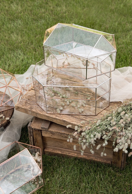 Caixas de vidro de casamento para envelopes de saudações em mesinha de madeira e o tecido branco com plantas como decoração