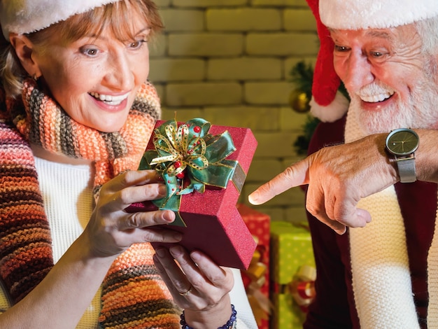 Una caja abierta de regalo de Navidad rojo se mantiene unido por una pareja caucásica senior borrosa con cara feliz de sorpresa. Celebración de navidad y año nuevo.