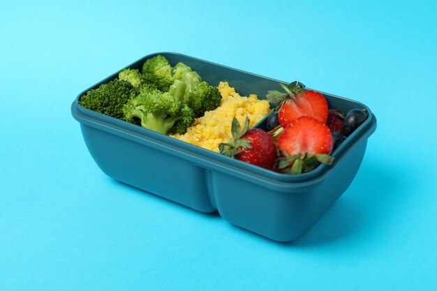 Caja de almuerzo con comida sabrosa sobre fondo azul.