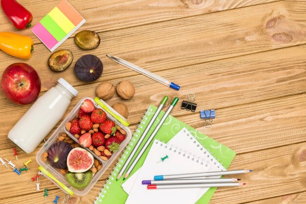 Caja de almuerzo nutritiva hecha de frutas bayas y nueces Botella de yogur de agua Mesa de madera ligera