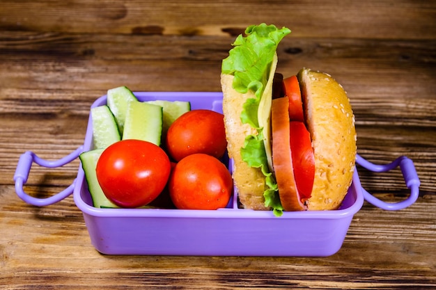 Caja de almuerzo con pepinos de hamburguesa y tomates en mesa de madera rústica