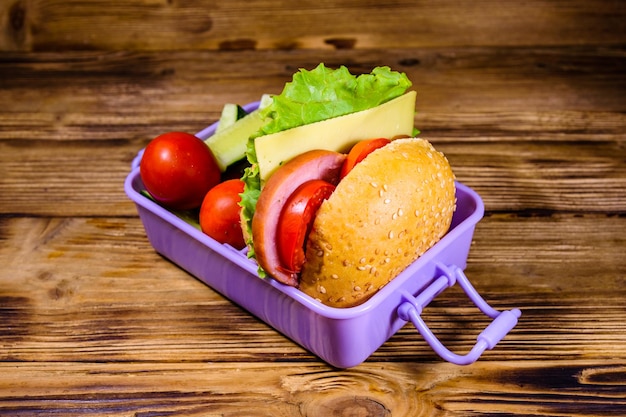 Caja de almuerzo con pepinos de hamburguesa y tomates en mesa de madera rústica