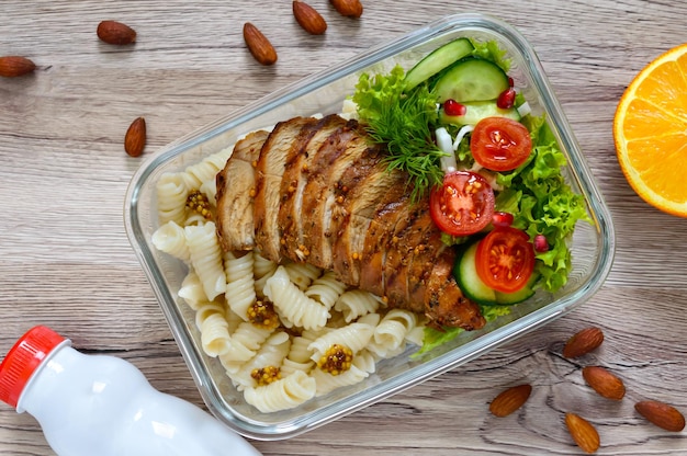 Caja de almuerzo: rotini con pechuga de pollo al horno y ensalada sobre un fondo de madera. Vista superior, endecha plana. Delicioso almuerzo saludable. El concepto de alimentación saludable.