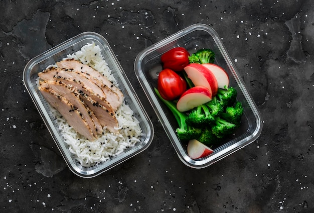 Caja de almuerzo saludable pastrami de pollo con tomates de brócoli de arroz y manzana en una vista superior de fondo oscuro