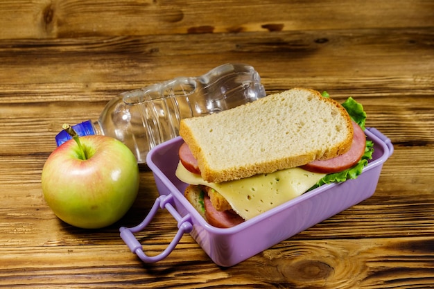 Foto caja de almuerzo con sándwiches botella de agua y manzana en una mesa de madera