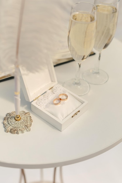 Una caja con anillos de boda y lentejuelas doradas, copas de champán, flores.