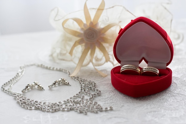 Caja con anillos de boda sobre la mesa junto con el collar y los pendientes Novia