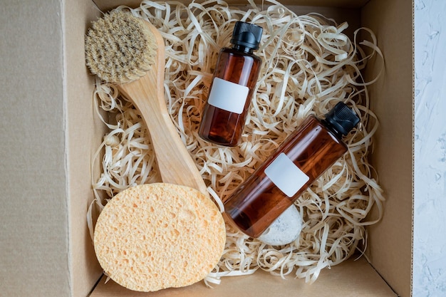 Foto caja de belleza con productos para el cuidado de la cara y el cuerpo sobre fondo gris botellas de loción aceite hidrofílico facial cepillo de madera y esponjas cosméticos naturales regalo