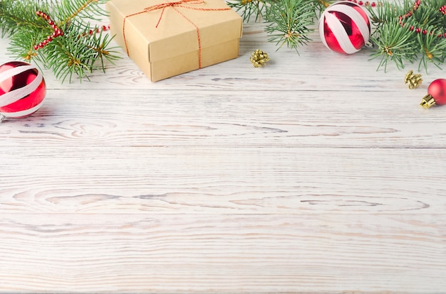 Caja de bolas de Navidad con un regalo y ramas de árboles de Navidad en madera blanca