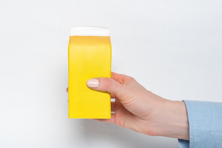 Foto caja de cartón amarilla o empaque de tetra pack en una mano femenina