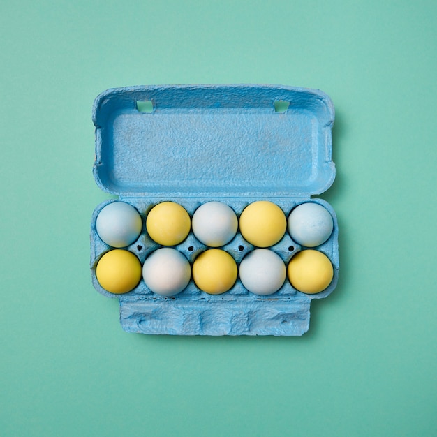 Caja de cartón azul con coloridos huevos de pascua pintados de amarillo y azul presentados sobre un fondo verde