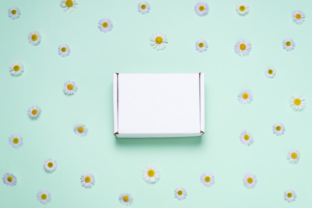 Caja de cartón blanco sobre fondo de color decorado con flores frescas