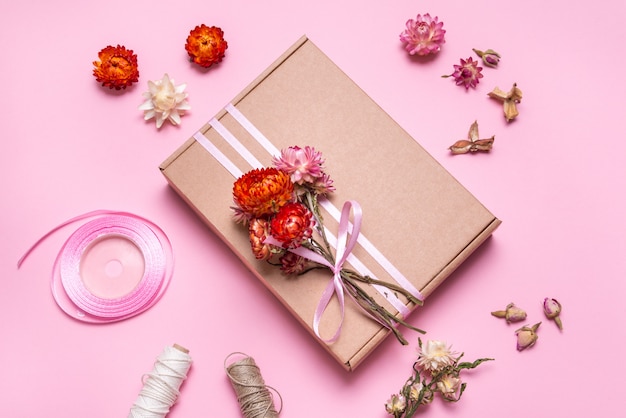 Caja de cartón decorada con flores secas en mesa rosa