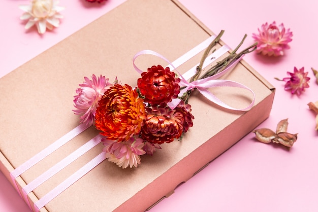 Caja de cartón decorada con flores secas en mesa rosa