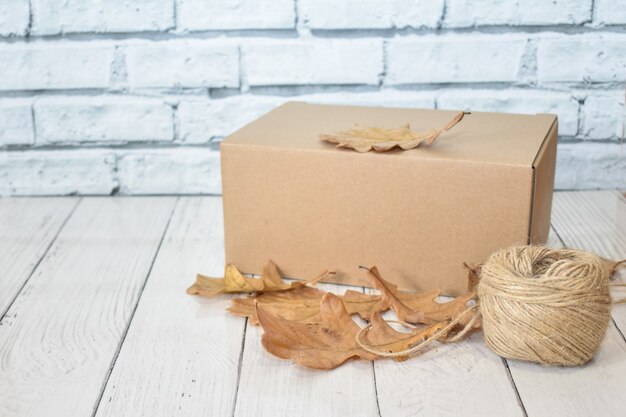 Caja de cartón, hojas de roble otoñal y bola de cuerda sobre fondo de mesa de madera y pared de ladrillo