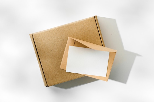 Caja de cartón marrón con un sobre en blanco sobre un fondo claro en un entorno bien iluminado