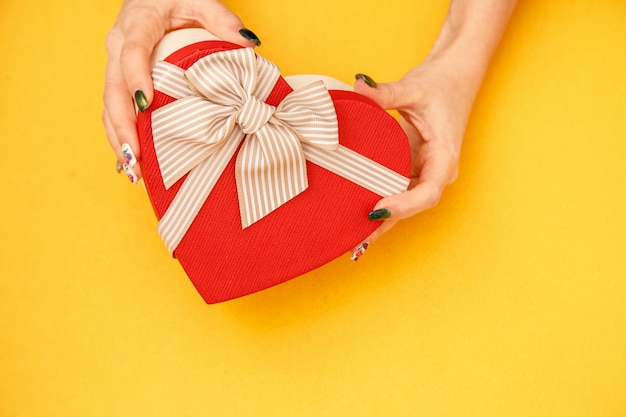 Caja de cartón de regalo biodegradable en forma de corazón en manos de mujeres