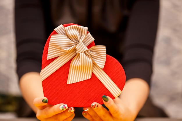 Caja de cartón de regalo biodegradable en forma de corazón en manos de mujeres