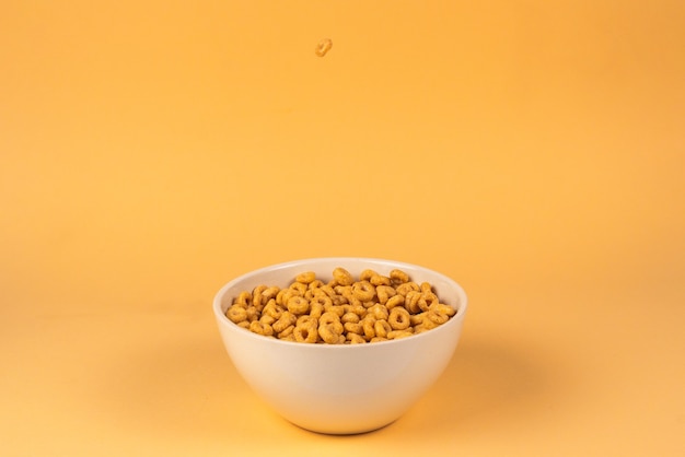 Caja de cereales de anillos de miel para el desayuno de la mañana. Copos de maíz cayendo al cuenco blanco. Movimiento. Copyspace.