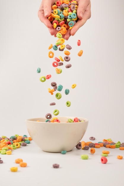 Caja de cereales de colores para el desayuno de la mañana. Copos de maíz cayendo al tazón blanco. Movimiento. Espacio de copia.