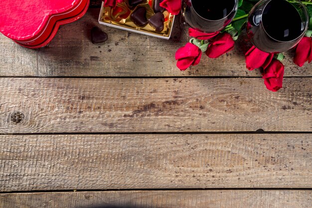 Caja de chocolate, rosas, copas de vino y corazón en mesa de madera