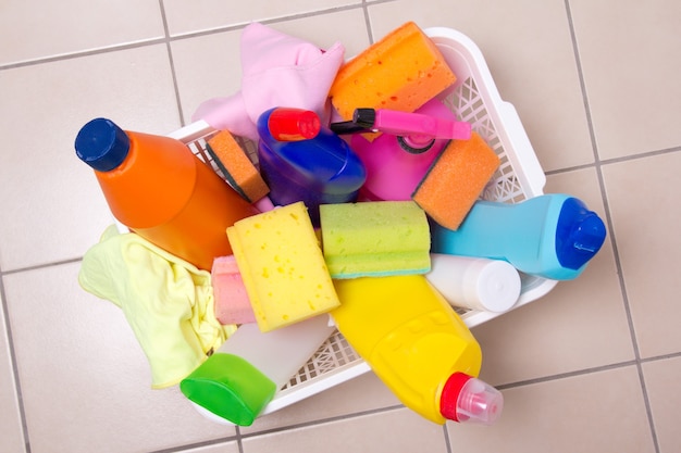 Caja completa de productos de limpieza sobre suelo de baldosas en el baño.