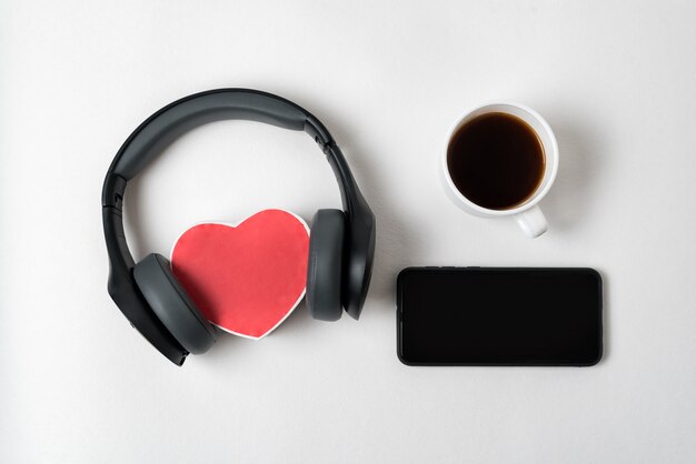 Caja de corazón con auriculares estéreo, teléfono inteligente y una taza de té en a. Vista superior copia espacio