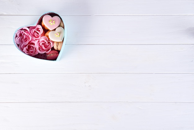 Caja de corazón con galletas y rosa sobre fondo blanco de madera, día de San Valentín