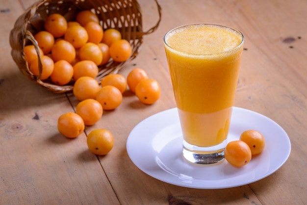 Cajá de frutas brasileiras. Copo de suco na mesa de madeira.