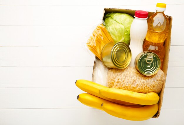 Caja de donación con comida sobre fondo blanco de madera