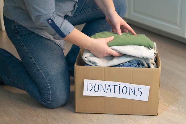 Foto la caja de donación de ropa no está en el suelo. las manos de la mujer doblan la ropa con cuidado. concepto de donación y caridad