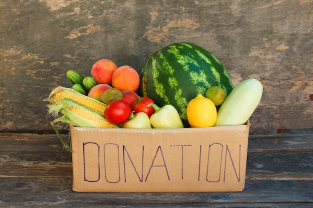 Caja de la donación con las verduras y las frutas en el viejo fondo de madera.