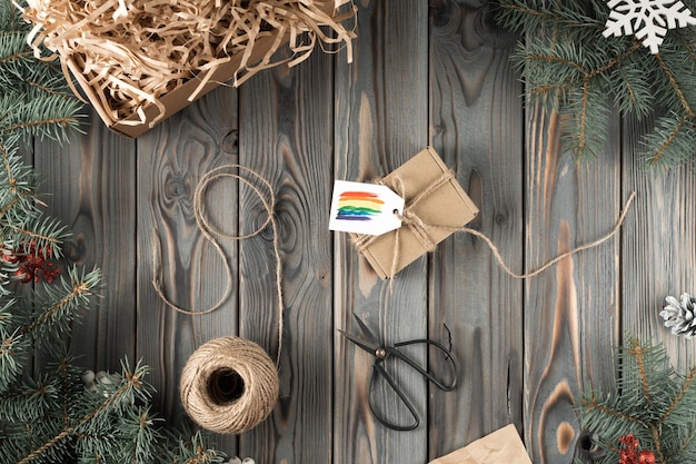 Caja envuelta artesanal de tela orgánica natural con tarjeta festiva de etiqueta de arco iris con manga de cuerda de tijeras sobre mesa de madera