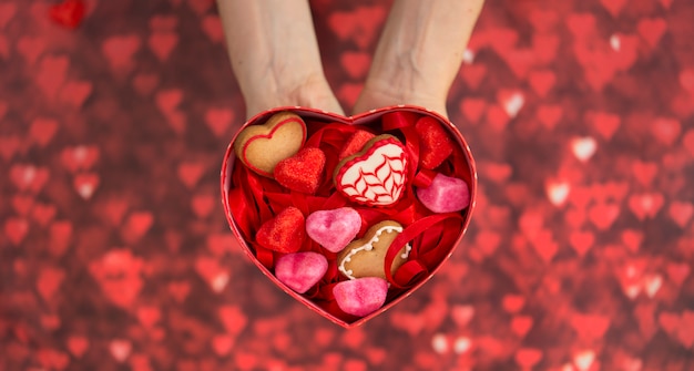 Foto caja en forma de corazón, con gominolas en forma de corazón, galletas en forma de corazón y fondo rojo