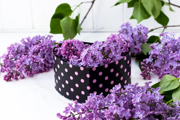 Una caja en forma de corazón con lilas dentro Hermosa caja negra con lunares rosas sobre un fondo blanco