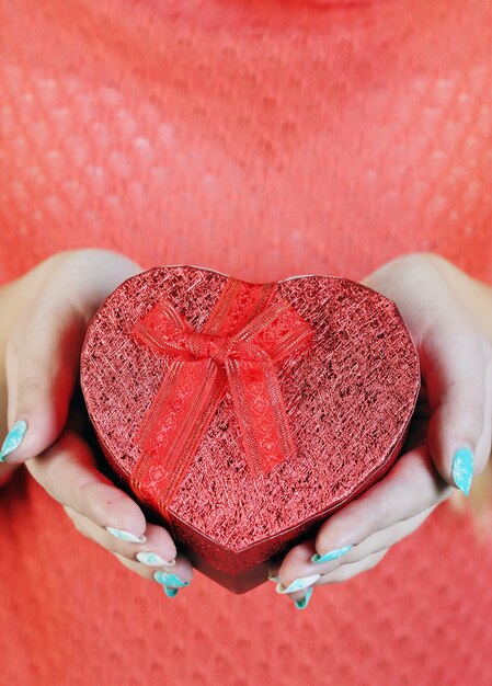 Caja en forma de corazón rojo en sus manos, close-up