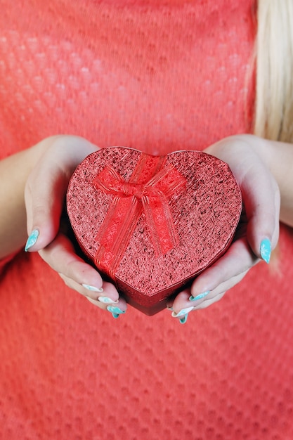 Caja en forma de corazón rojo en sus manos, close-up