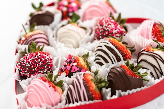 Caja en forma de corazón con una variedad de fresas cubiertas de chocolate sobre un fondo blanco.