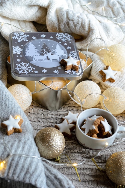 Una caja con una guirnalda de Año Nuevo y una taza con estrellas de pan de jengibre sobre una manta tejida